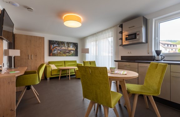 Moderner Wohn- und Essbereich mit grünen Stühlen, Sofa, Holzmöbeln und Küchenzeile mit Mikrowelle