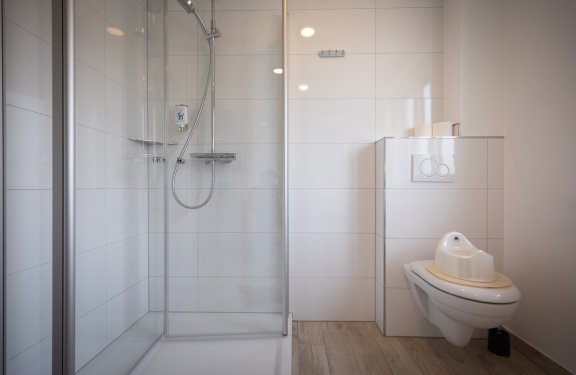 Helles Badezimmer mit Duschkabine links und Toilette mit Kindersitz rechts