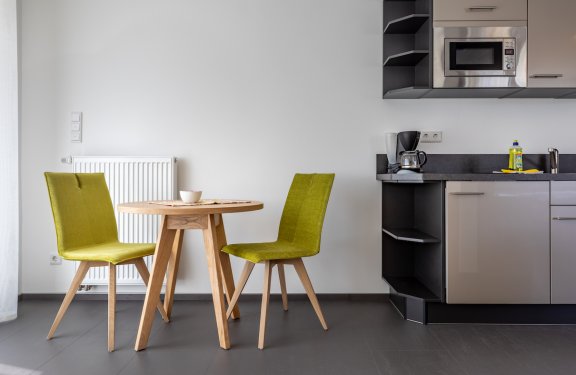 Kleine Küche mit runden Holztisch, zwei grünen Stühlen und Kaffeemaschine auf der Arbeitsplatte