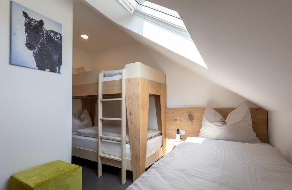 Schlafzimmer mit Etagenbett und Einzelbett unter Dachschräge, grüner Hocker und Bild an der Wand