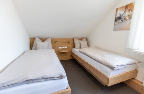 Zwei Einzelbetten mit weißen Bettwäsche und Holzkopfteil in einem hellen Zimmer mit Dachschräge