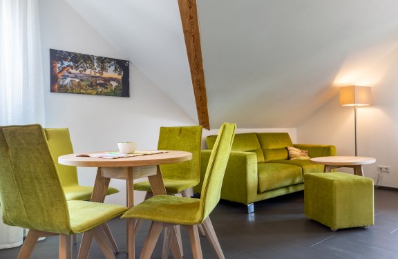 Grünes Sofa und Stühle um runden Holztisch in modernem Wohnzimmer mit Dachschräge