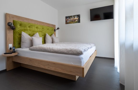 Modernes Schlafzimmer mit Holzrahmenbett, grünem Kopfteil, weißen Kissen und Wand-TV