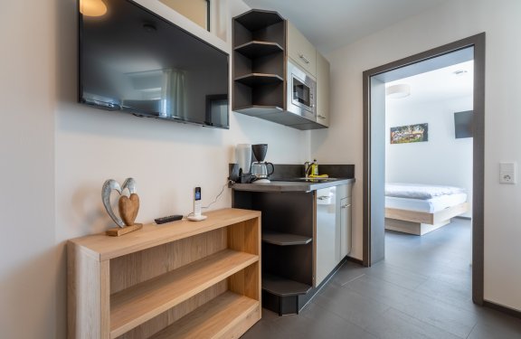 Kleine Küchenzeile mit Mikrowelle, Kaffeemaschine und Fernseher, Blick ins Schlafzimmer