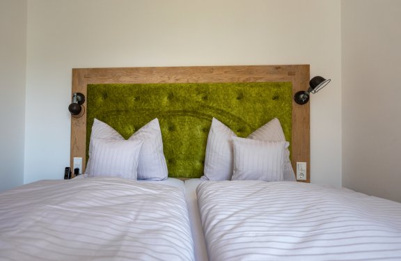 Doppelbett mit grünem gepolstertem Kopfteil und weißen gestreiften Bettdecken und Kissen