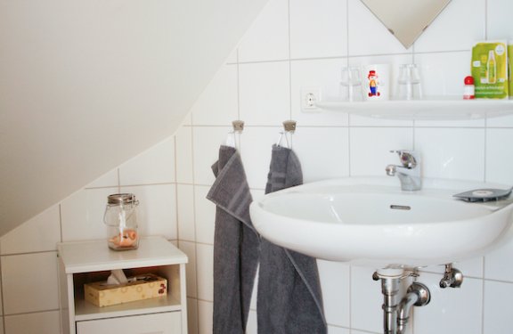 Kleines Badezimmer mit weißem Waschbecken, zwei grauen Handtüchern und einem kleinen Schrank unter einer Dachschräge